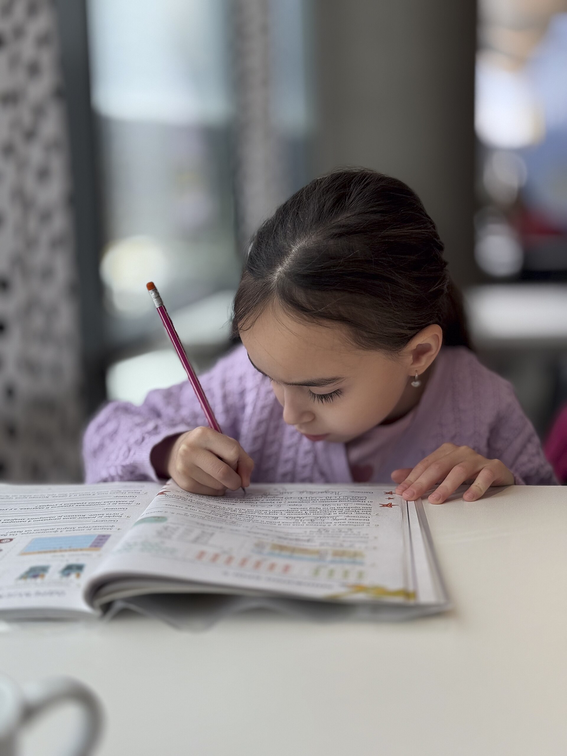 Una nena concentrada escribe con un lápiz en un cuaderno sobre la mesa